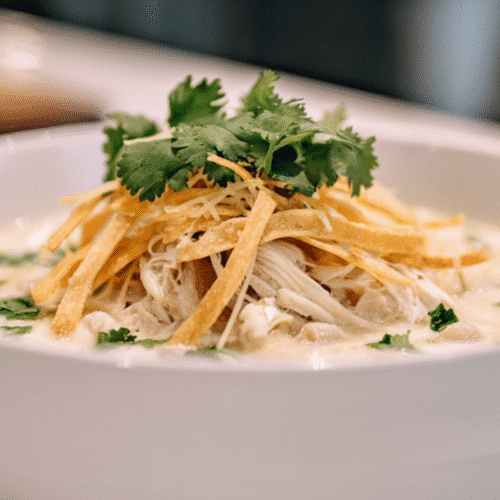 Creamy white chicken chili in a white bowl topped with shredded chicken, crispy tortilla strips, melted cheese, and fresh cilantro.
