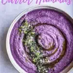 Bowl of creamy carrot hummus served with fresh vegetables and pita bread