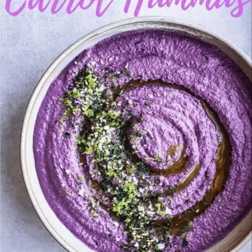 Bowl of creamy carrot hummus served with fresh vegetables and pita bread