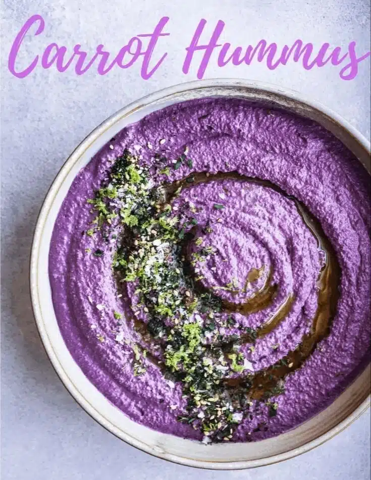 Bowl of creamy carrot hummus served with fresh vegetables and pita bread