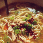 A bowl of Classic Ginger Garlic Chicken Soup with noodles garnished with green onions.