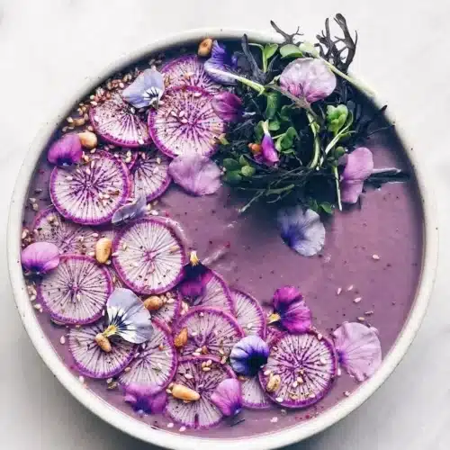 Bowl of purple cauliflower fennel ginger soup garnished with herbs