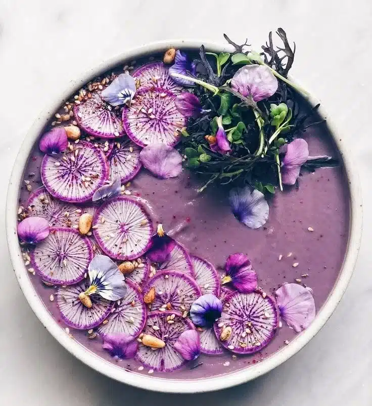 Bowl of purple cauliflower fennel ginger soup garnished with herbs