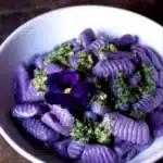 Plate of purple potato gnocchi topped with walnut pesto, showcasing a colorful dish.