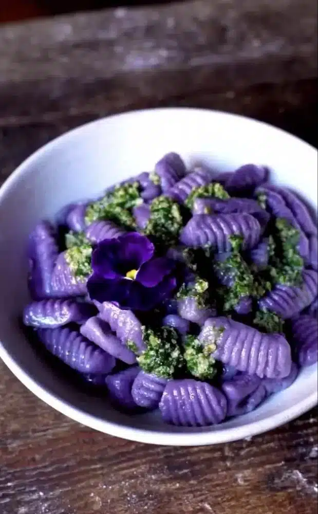 Plate of purple potato gnocchi topped with walnut pesto, showcasing a colorful dish.