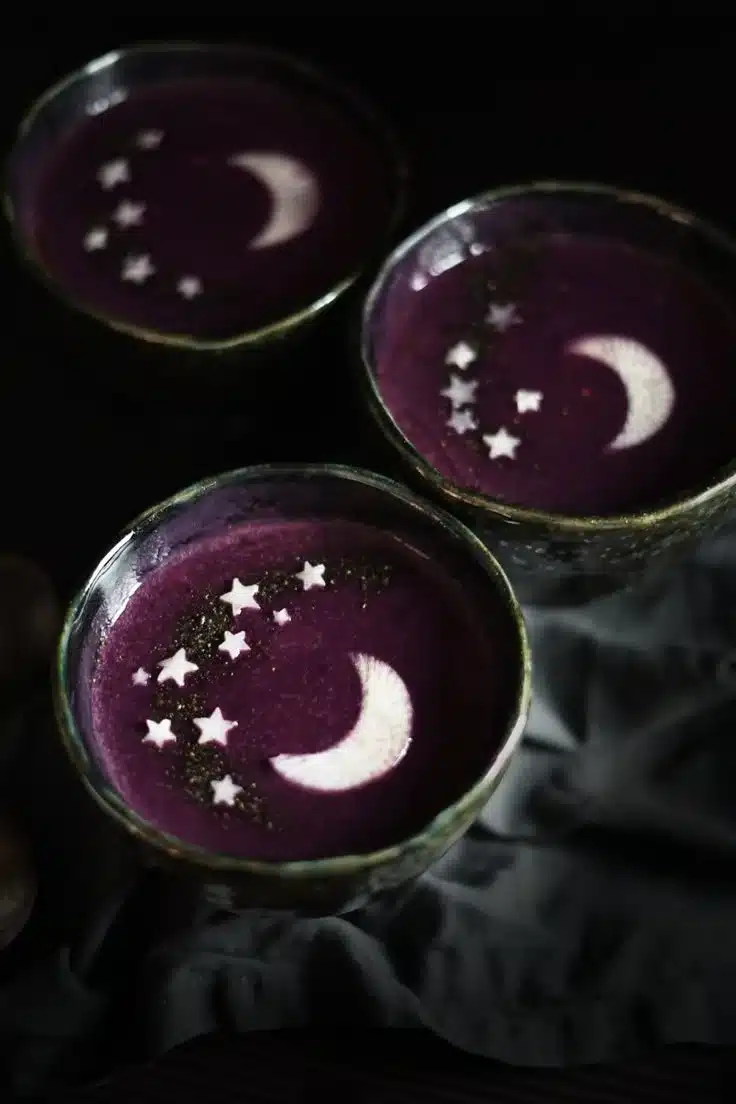 Bowl of velvety purple soup garnished with herbs and vegetables.