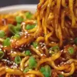 Plate of sticky chicken noodles garnished with herbs and vegetables